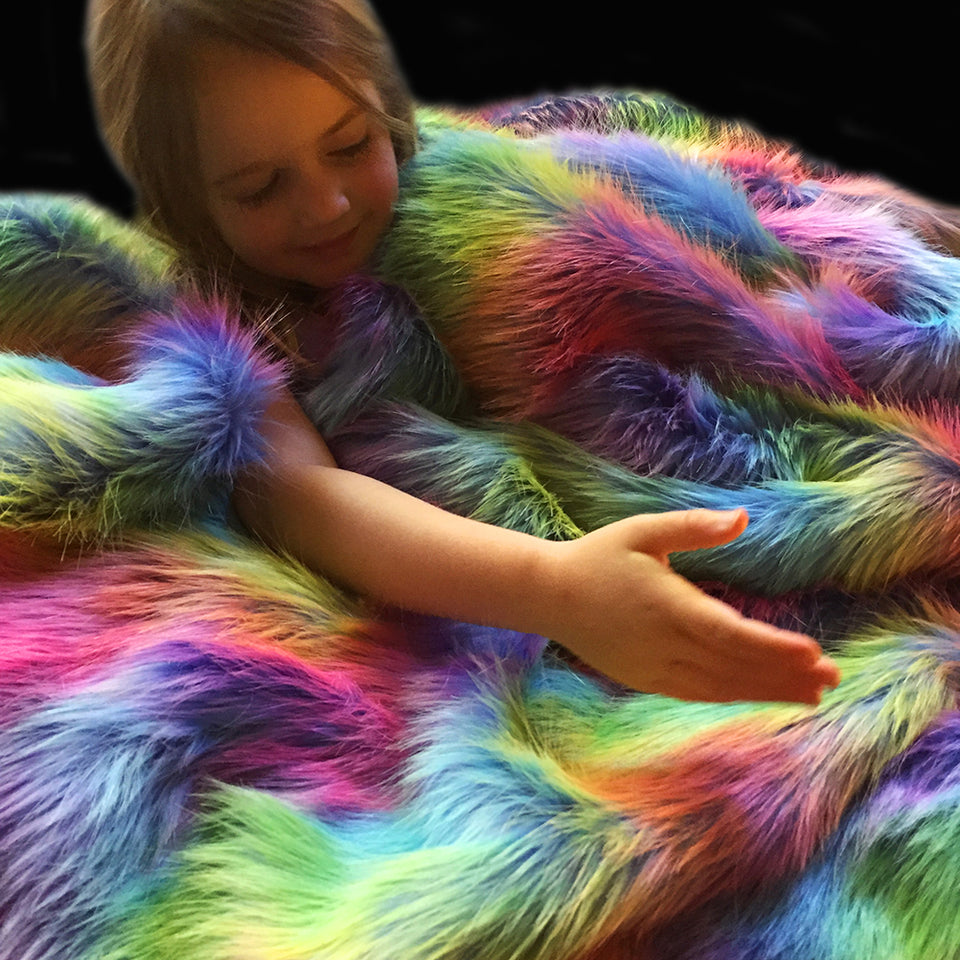 Colourful rainbow weighted throw blanket with child immersed in the soft faux fur textures. Weighted blanket made and designed by Happy Senses, Australia.